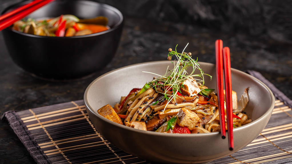 das Konzept der japanischen Küche. Chinesische Nudeln mit Huhn, gegrilltem Gemüse und Tofu in Unagi-Sauce. serviert asiatische Gerichte im Restaurant in einem Teller auf einer Bambusmatte. Ansicht von oben, Kopierraum - Foto, Bild
