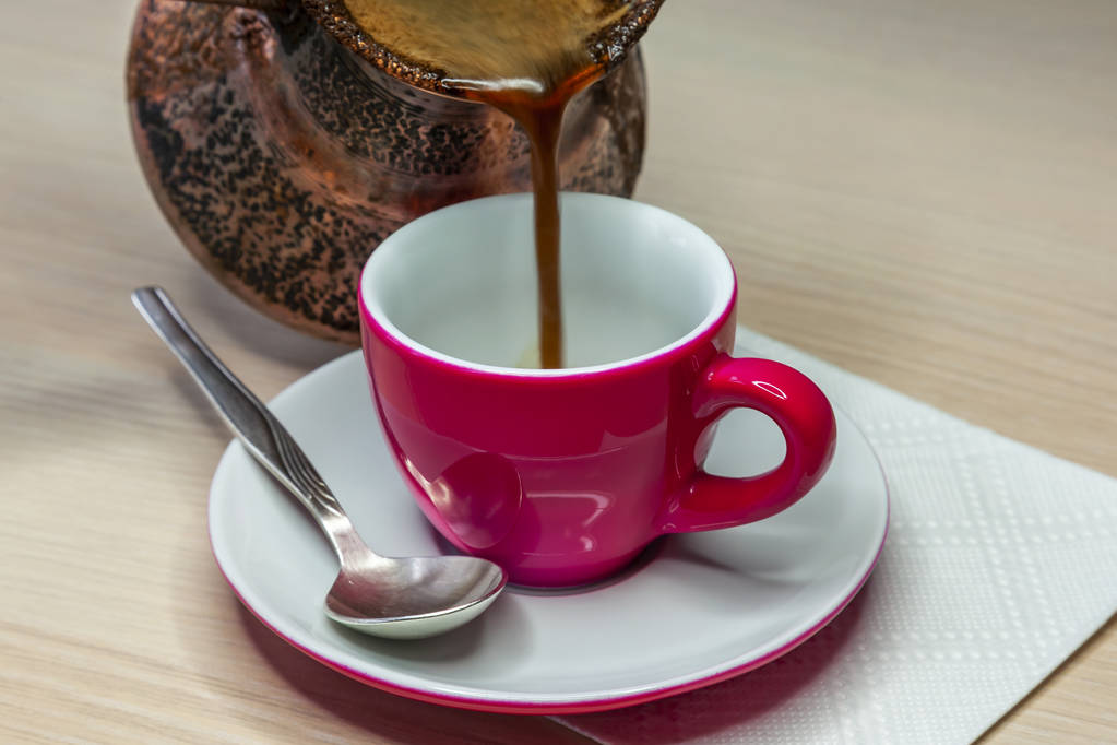 Il caffè nero scorre da un cezve in una tazza di caffè rosa brillante
 - Foto, immagini