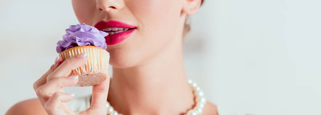 gedeeltelijke weergave van pin-up girl proeven zelfgemaakte cupcake met paarse crème  - Foto, afbeelding