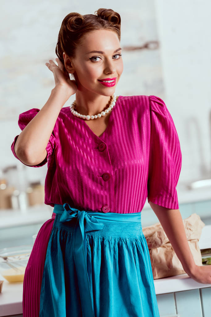 stylisches Pin Up Mädchen in purpurrotem Kleid und Perlenkette verbessert Frisur  - Foto, Bild