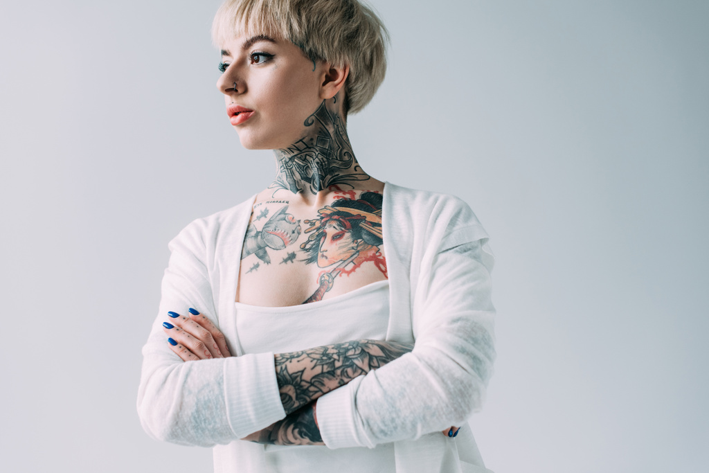 attraente donna con tatuaggi in piedi con le braccia incrociate isolato su grigio
 - Foto, immagini