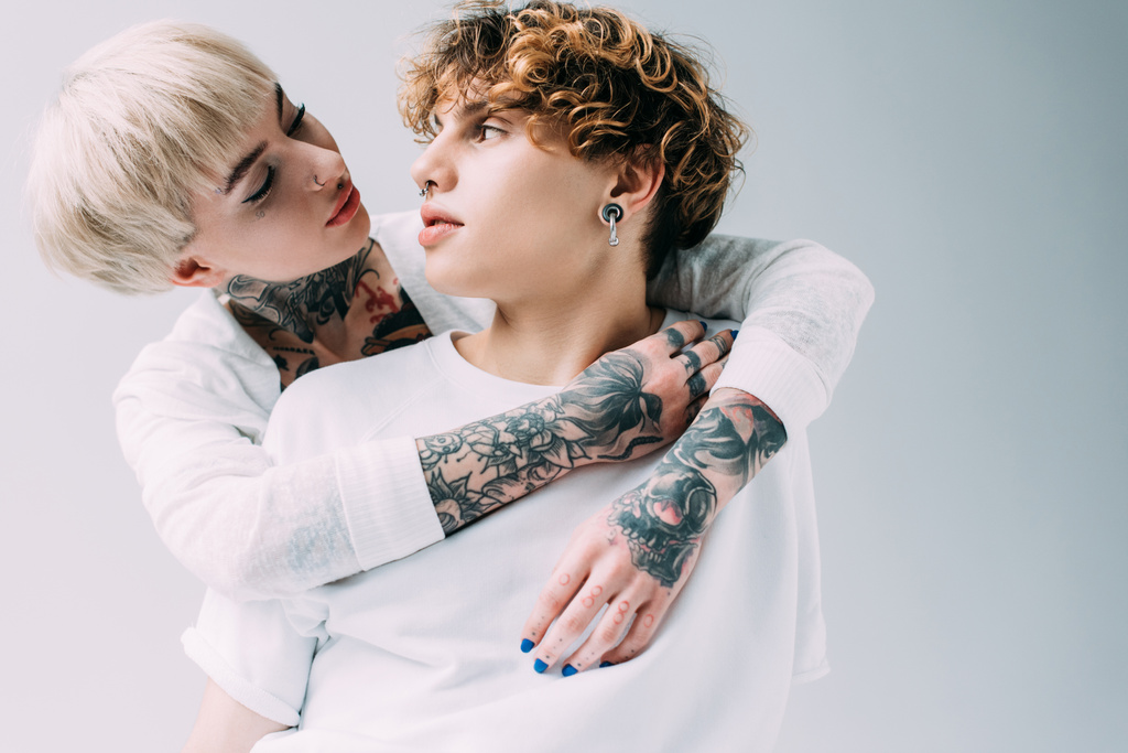 blonde girl with tattoos looking at boyfriend with curly hair isolated on grey - Photo, Image