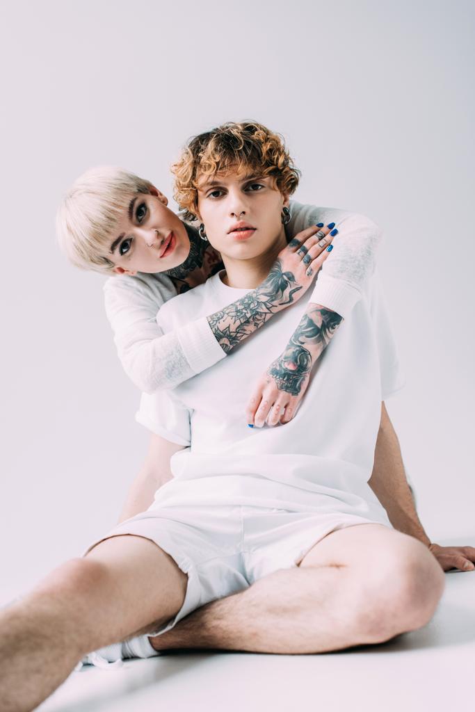 blondi nainen tatuoinnit halaus poikaystävä kihara tukka eristetty harmaa
 - Valokuva, kuva