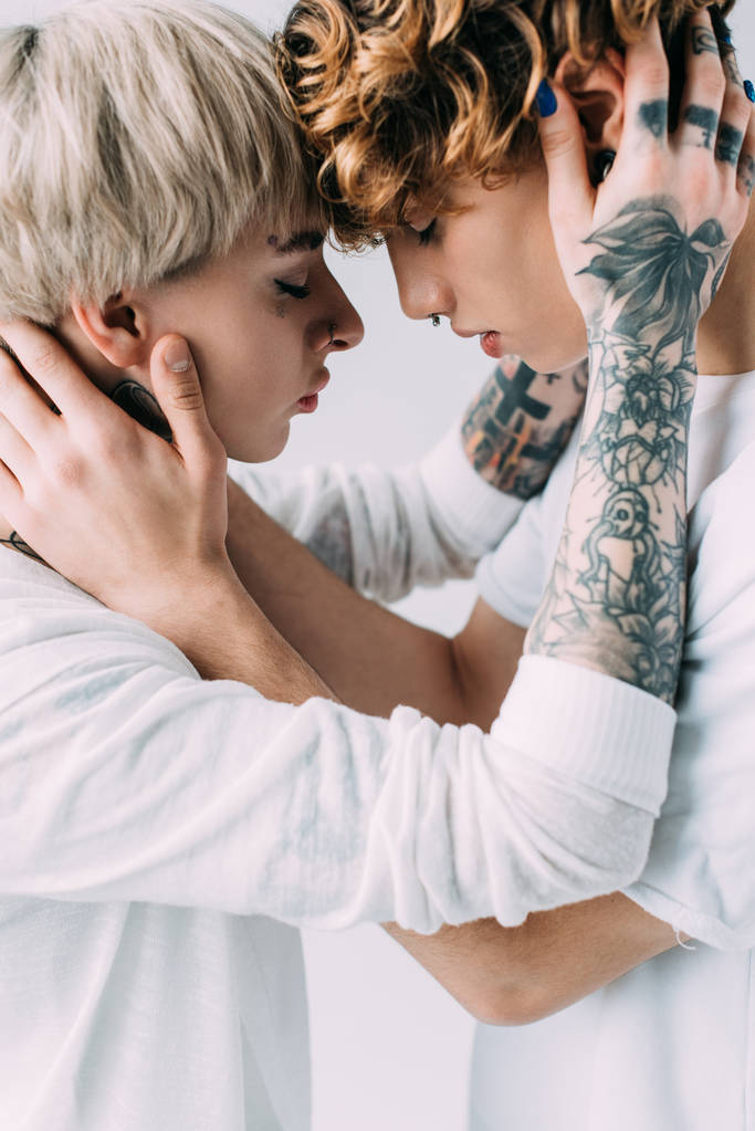 girlfriend with tattoos embracing boyfriend with curly hair isolated on grey  - Photo, Image