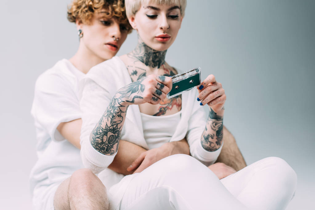 selektywne focus Blondynka tatuażem kobietę taśmy audio siedząc z chłopakiem na szarym tle  - Zdjęcie, obraz