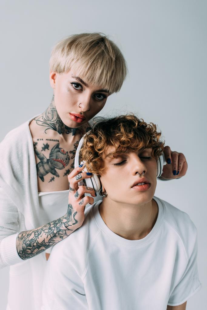 houkutteleva blondi tyttö tatuoinnit tilalla kuulokkeet mies suljetut silmät kuunnella musiikkia eristetty harmaa
  - Valokuva, kuva