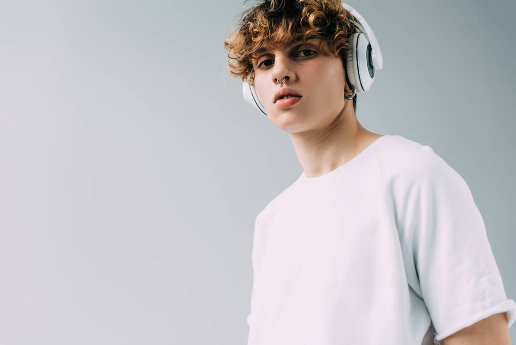 handsome man with curly hair listening music in headphones isolated on grey  - Photo, Image