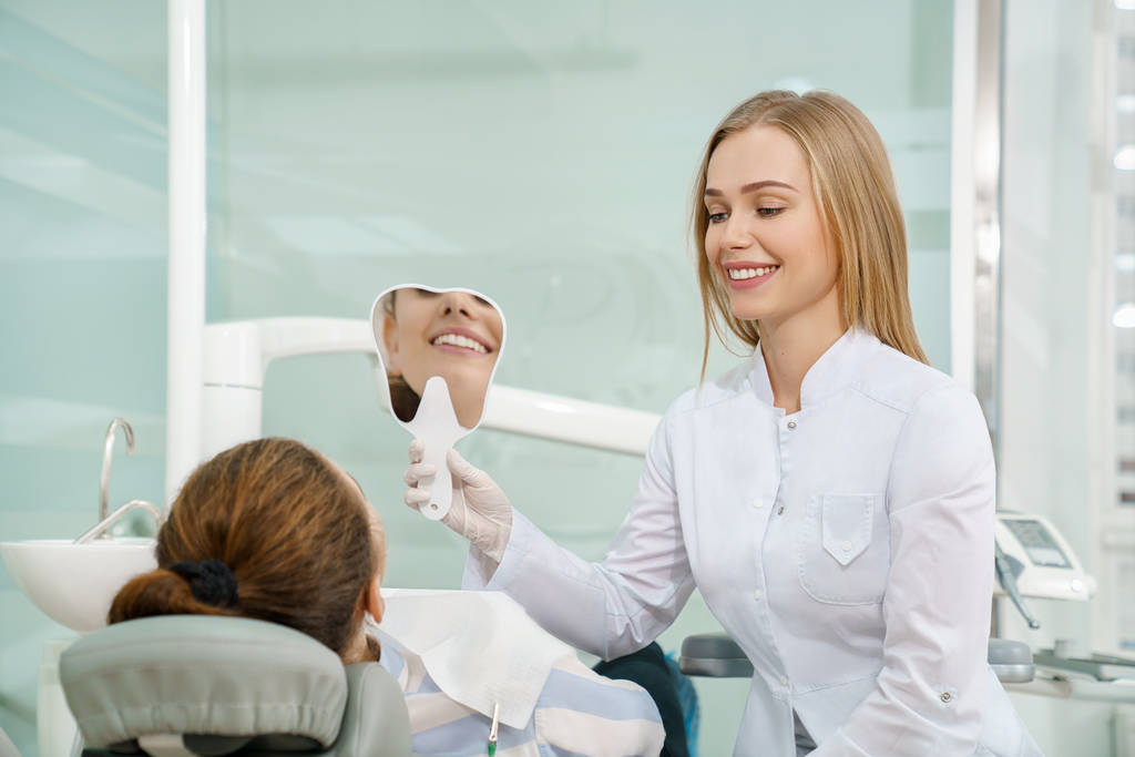 Dentista manteniendo espejo y mostrando al cliente una hermosa sonrisa
 - Foto, imagen