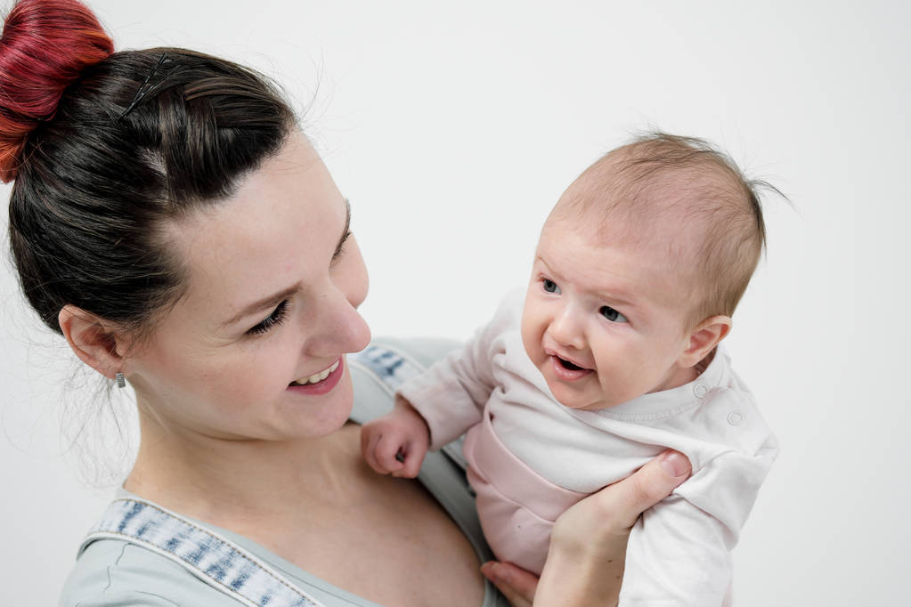Mujer joven madre en overoles de mezclilla sostiene a un bebé en sus brazos. Fondo blanco en el estudio
. - Foto, imagen