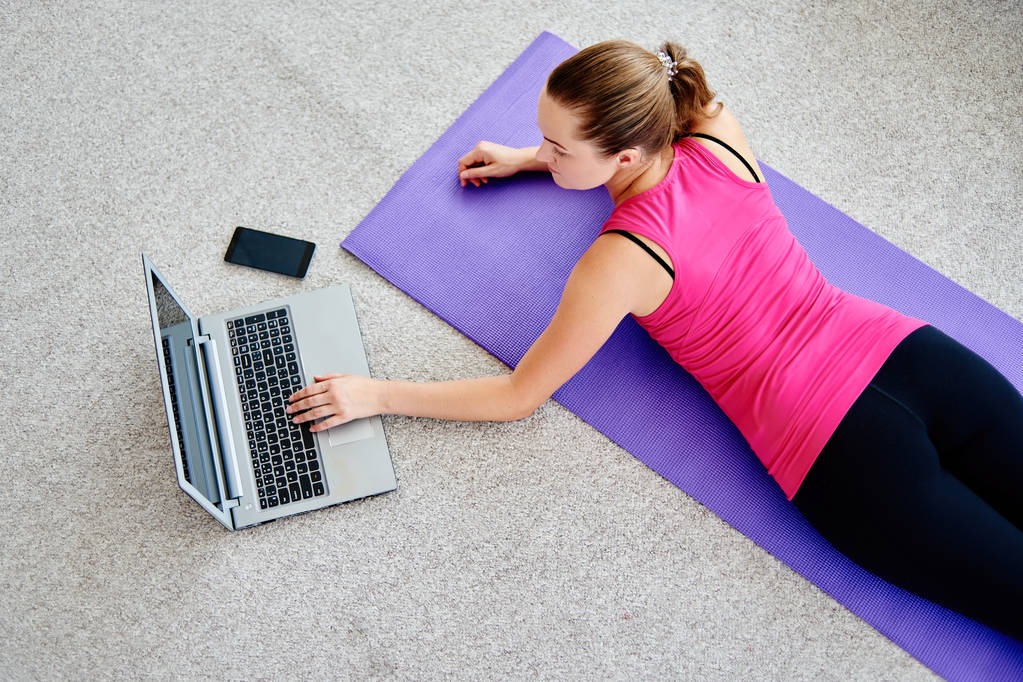 Mooie jonge vrouw doen werken oefening op vloer thuis en het gebruik van de laptop, on line training, kopie ruimte. Yoga, pilates, uit te oefenen. Sport, gezonde levensstijl concept  - Foto, afbeelding