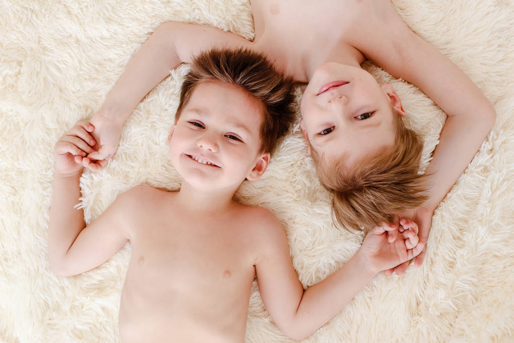 zwei lächelnde Jungen liegen auf dem Rücken auf einer weißen, flauschigen Decke, Draufsicht - Foto, Bild