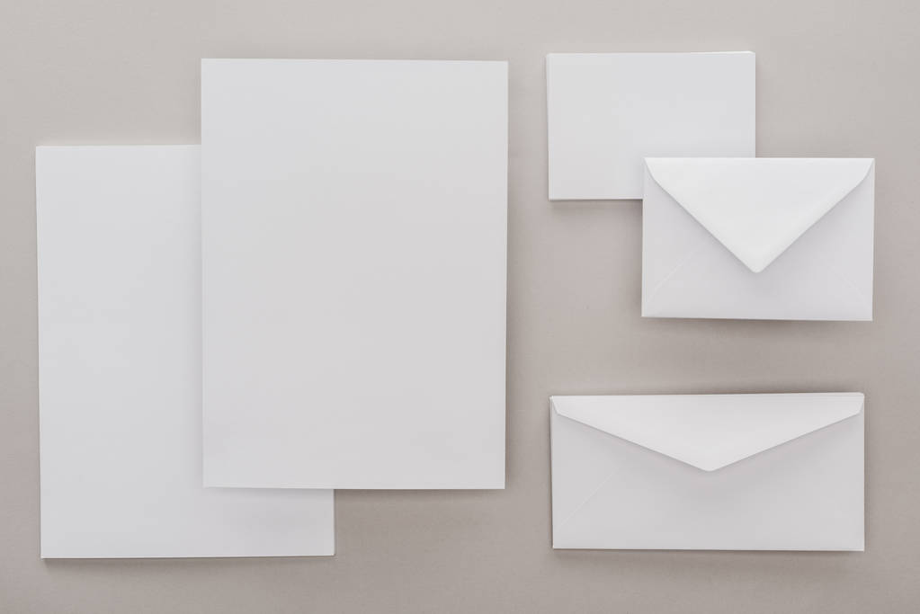 vlakke leggen met witte blanco papier en enveloppen op grijze achtergrond - Foto, afbeelding