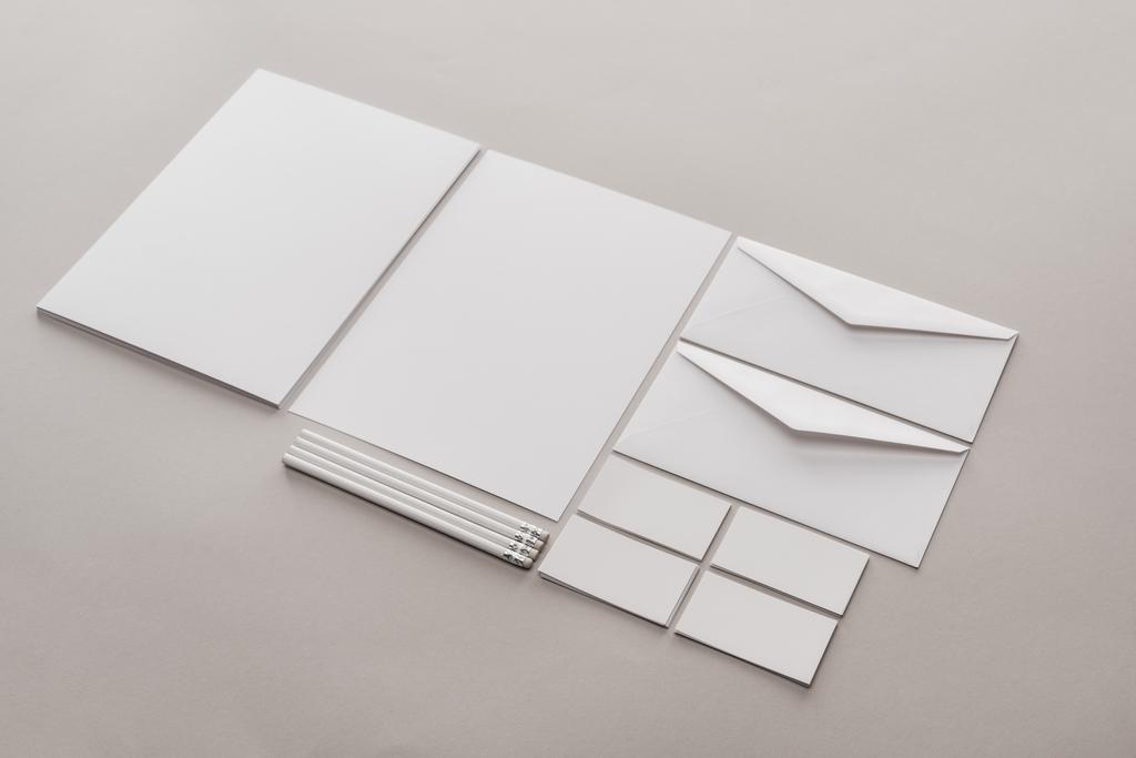 flache Lage mit weißen leeren Papieren, Karten, Umschlägen und Bleistiften auf grauem Hintergrund - Foto, Bild
