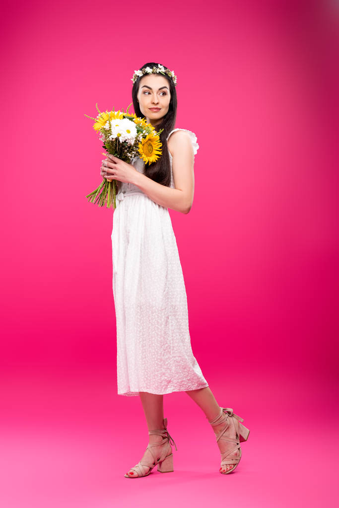 vista completa de la hermosa mujer morena en vestido blanco y corona floral con ramo de flores en rosa
 - Foto, Imagen