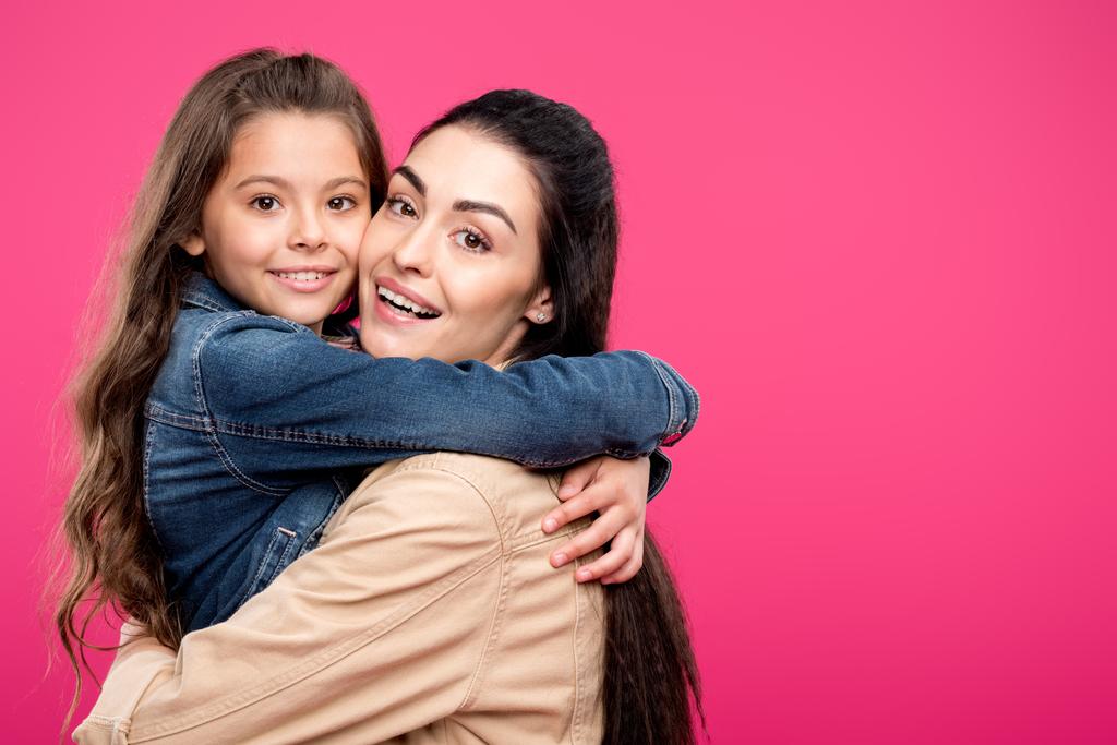 schöne Mutter und Tochter umarmen und lächeln in die Kamera isoliert auf rosa   - Foto, Bild