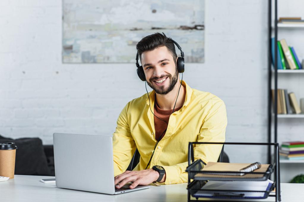 Empresário barbudo sorridente ouvindo música e olhando para a câmera no escritório
 - Foto, Imagem
