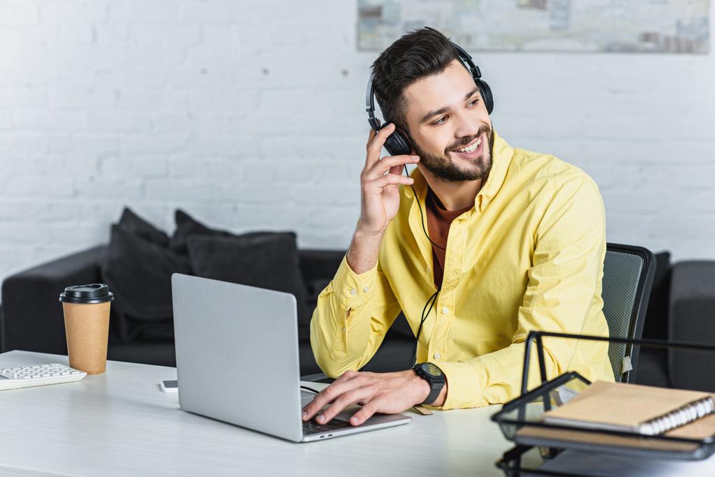 Sonriente hombre de negocios barbudo escuchando música y mirando hacia otro lado
  - Foto, Imagen
