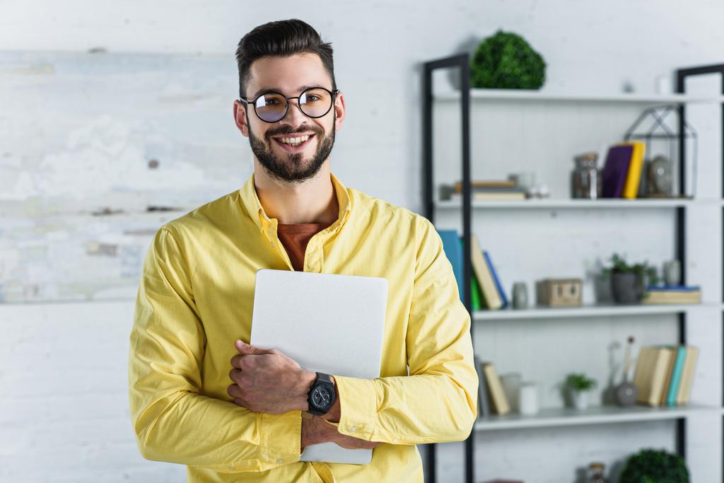 Hombre de negocios sonriente con gafas sosteniendo la tableta digital y mirando a la cámara en la oficina
 - Foto, Imagen