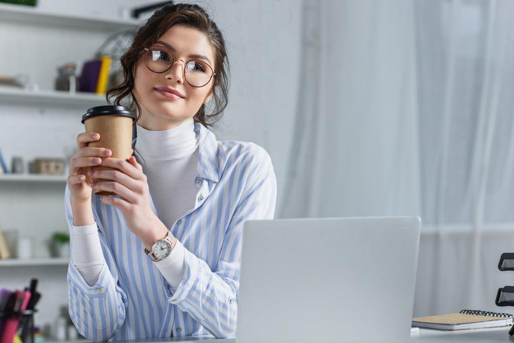 Belle femme d'affaires tenant tasse en papier et regardant loin au lieu de travail
 - Photo, image