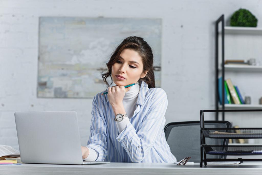 Focused attractive businesswoman holding pencil and looking at laptop - Photo, Image