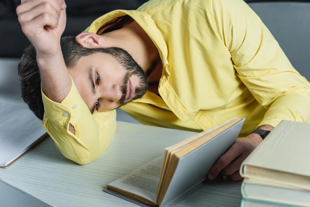 втомлений чоловік навчається з книгою, лежачи на столі в сучасному офісі
  - Фото, зображення
