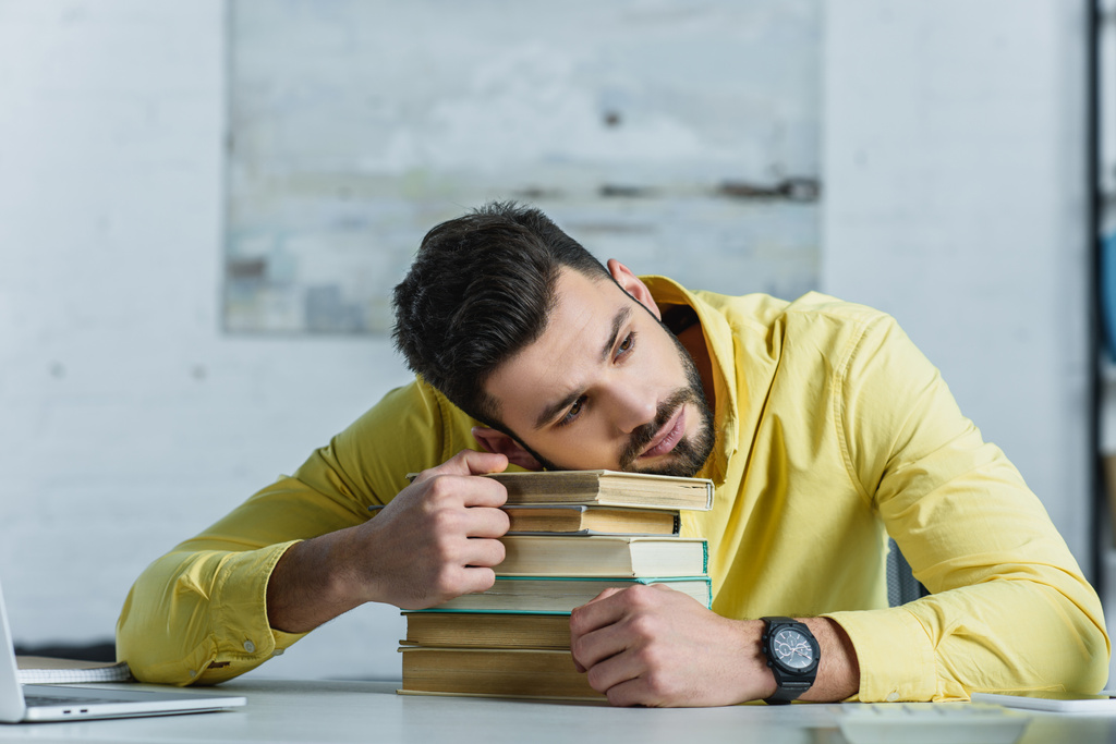 ένας άνθρωπος κουρασμένος, που βρίσκεται στα βιβλία στο σύγχρονο γραφείο  - Φωτογραφία, εικόνα