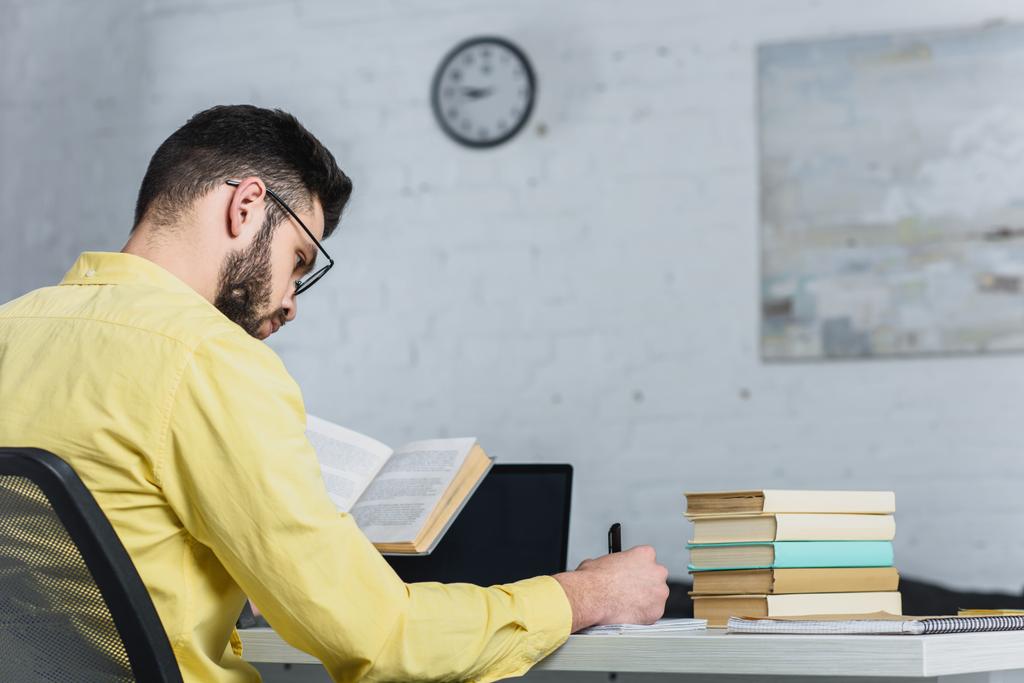 foco seletivo do homem escrevendo enquanto segurando livro no escritório moderno
 - Foto, Imagem