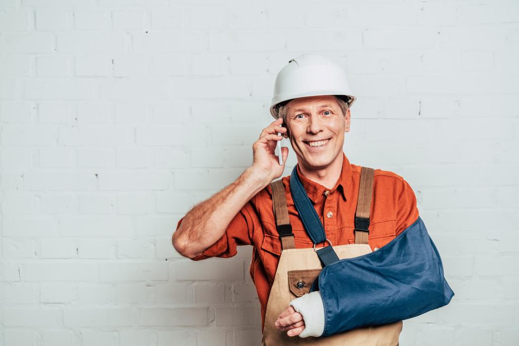 repairman with arm bandage talking on smartphone at white textured background - Photo, Image