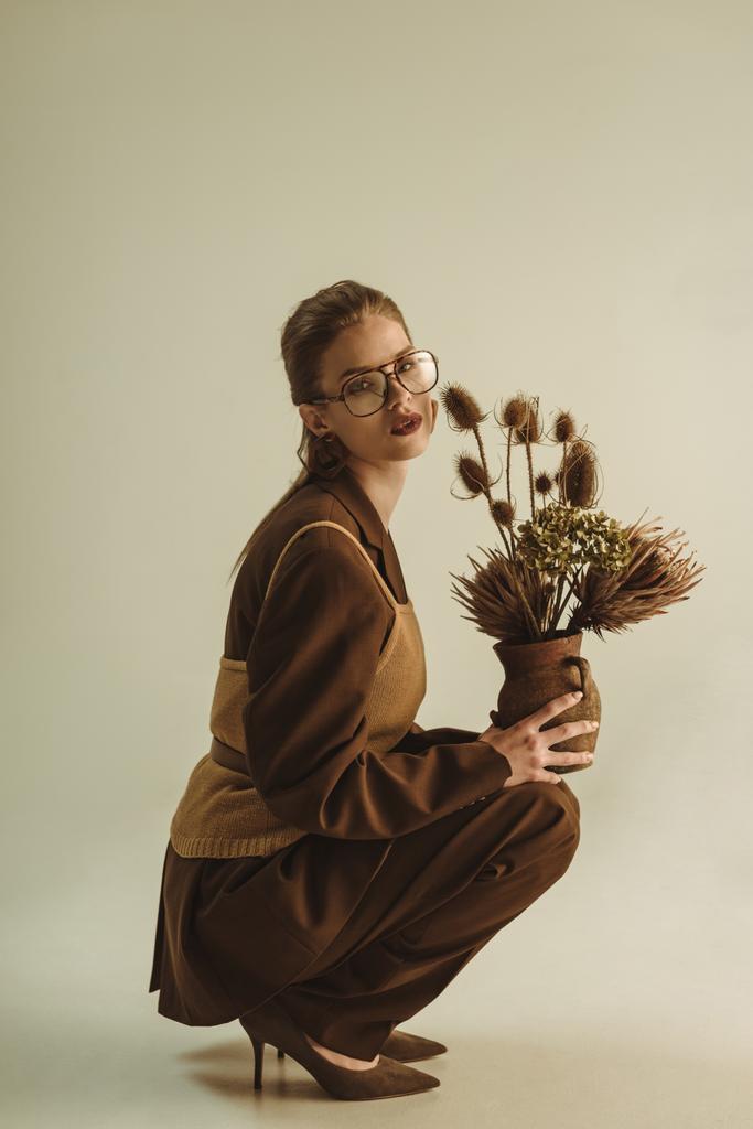 elegante ragazza in possesso di brocca di argilla con fiori secchi su beige
 - Foto, immagini