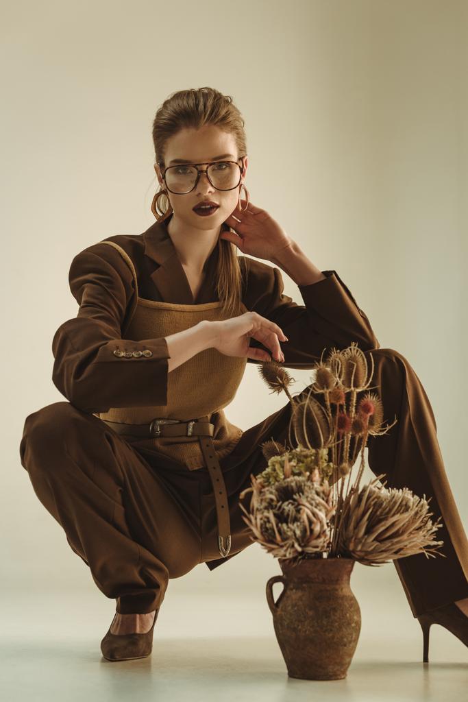 bella donna alla moda che tiene la brocca di argilla con fiori secchi su beige
 - Foto, immagini