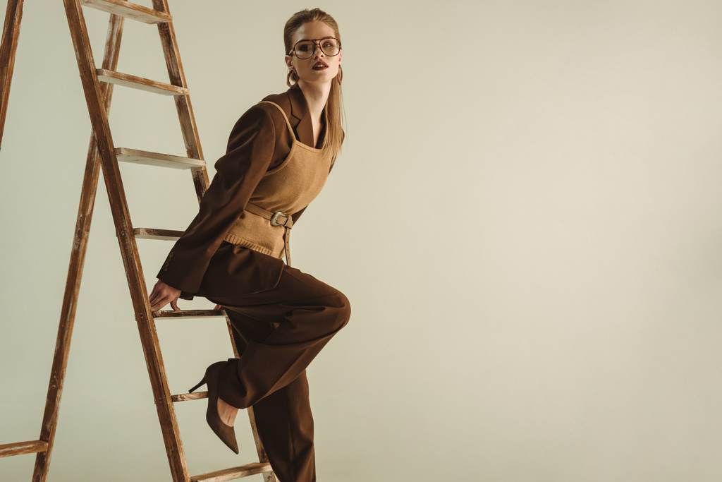 modelo atractivo en estilo retro posando cerca de escalera de madera aislada en beige
 - Foto, imagen