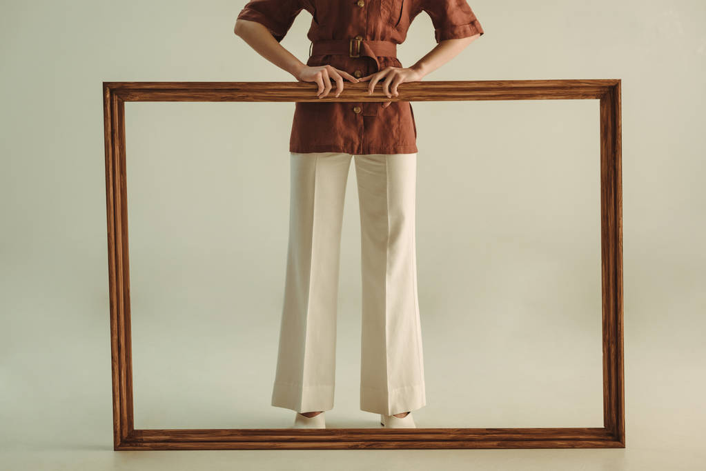 oříznutý pohled stylové ženy ve stylu vintage pózuje s velkým dřevěným rámem izolované na béžové - Fotografie, Obrázek