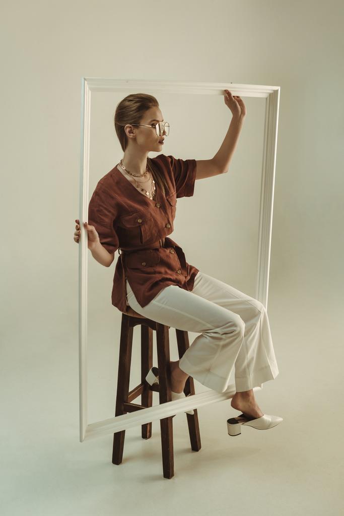 attraktive Frau posiert auf Hocker mit großem weißen Rahmen - Foto, Bild