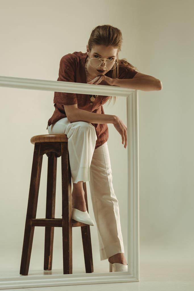 attraente donna alla moda in posa su sgabello con grande cornice bianca
 - Foto, immagini