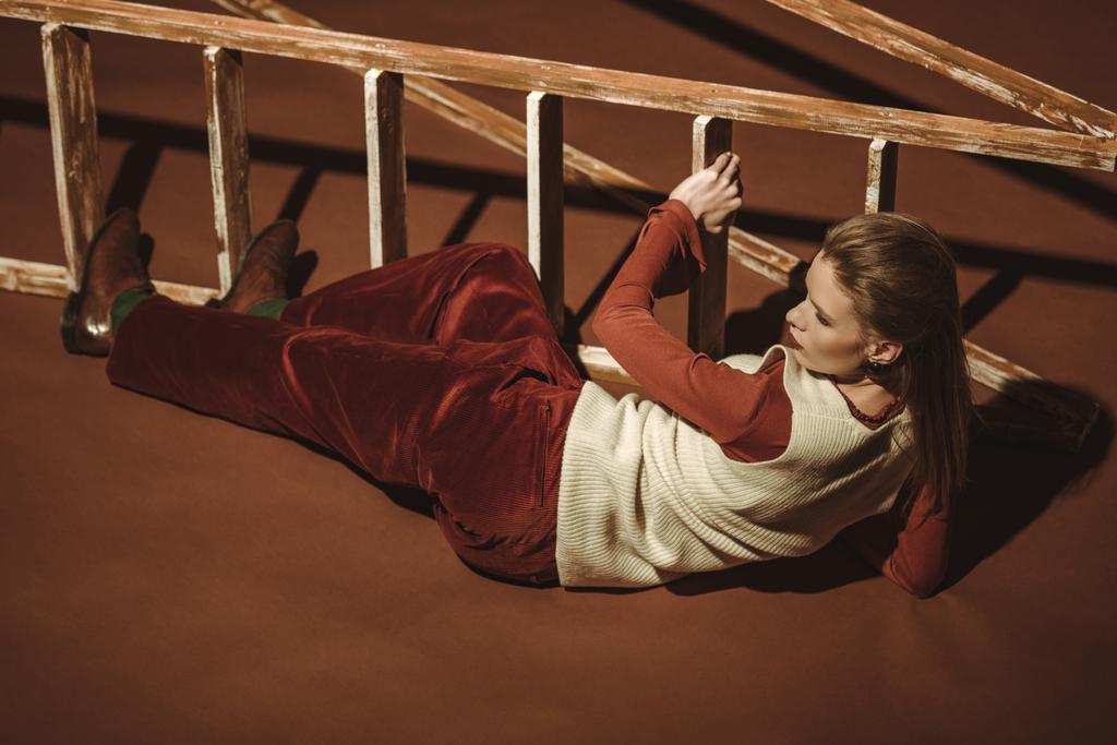 レトロなスタイルのブラウンの木製のはしごに近いポーズで魅力的な女の子 - 写真・画像