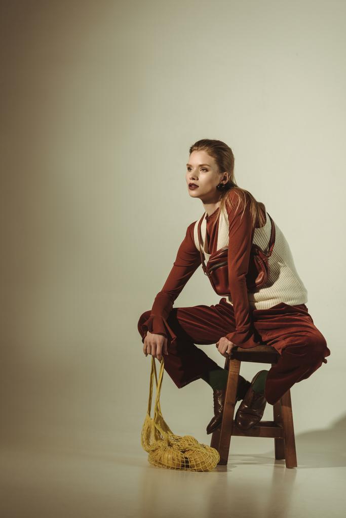 mulher elegante atraente sentado no banquinho com limões em saco de corda no bege
 - Foto, Imagem