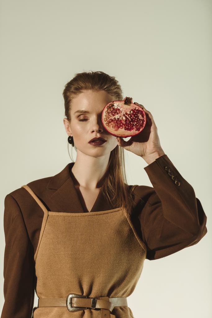 atraktivní žena se zavřenýma očima, hospodářství, polovina z granátového jablka před čelbou, izolované na béžové - Fotografie, Obrázek