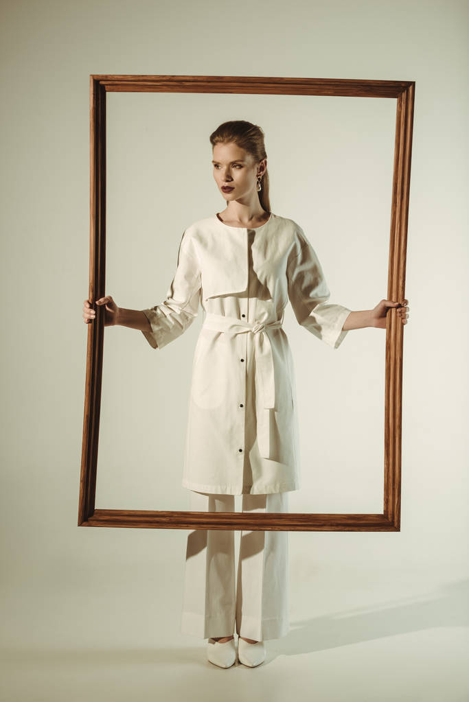 όμορφη μόδας γυναίκα σε λευκή στολή ποζάρει με μεγάλο ξύλινο πλαίσιο - Φωτογραφία, εικόνα
