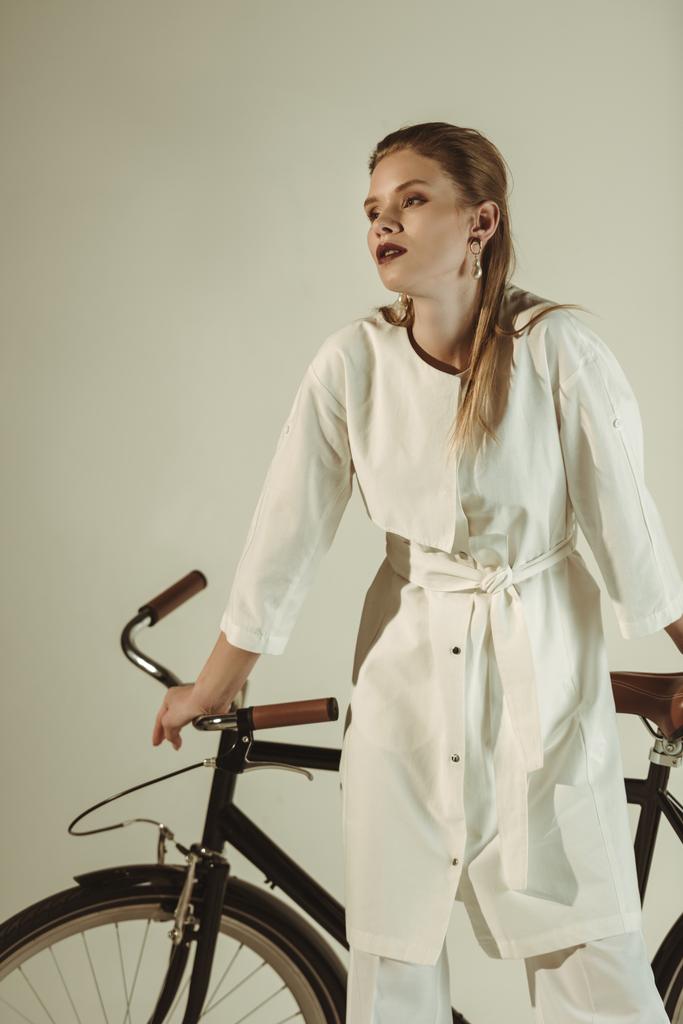 fashionable girl in white outfit posing on bicycle isolated on beige - Photo, Image