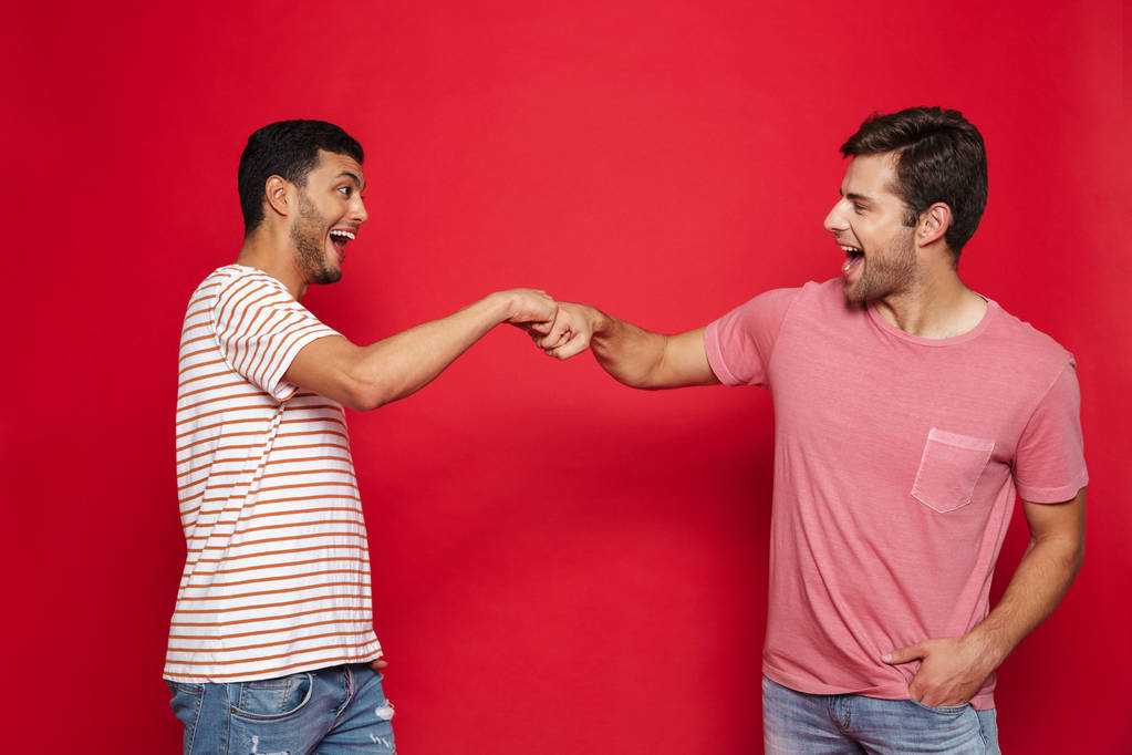 Два веселых молодых человека, стоящих в изоляции на красном фоне, давая кулак удара
 - Фото, изображение