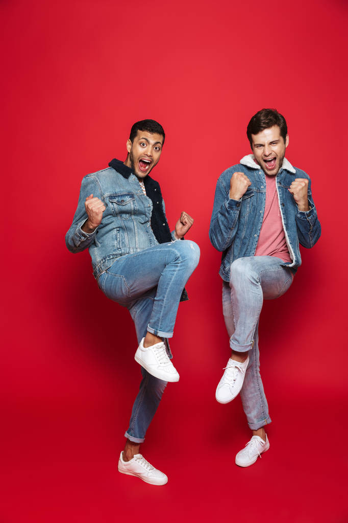Zwei gut gelaunte junge Männer springen vereinzelt über roten Hintergrund und feiern den Erfolg - Foto, Bild