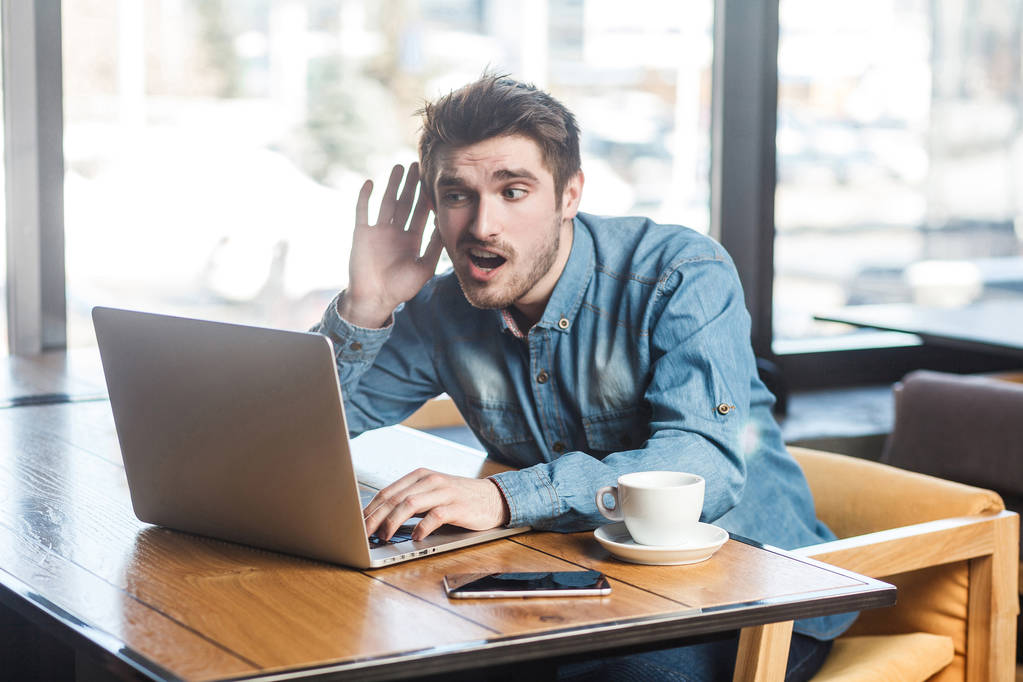 portret freelancer w blue jeans koszula siedząc w kawiarni i trzymając rękę w pobliżu ucha i stara się słyszeć rozmowy wideo na laptopie - Zdjęcie, obraz