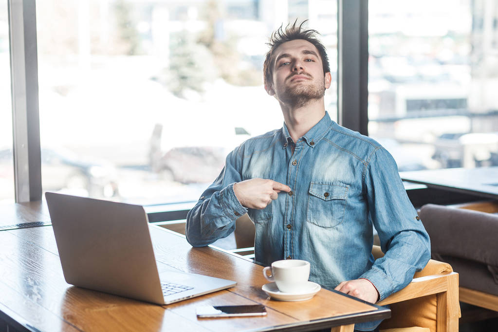 Retrato de confiante egoísta freelancer egoísta em camisa jeans azul sentado no café com laptop e apontando o dedo para si mesmo com orgulho
  - Foto, Imagem