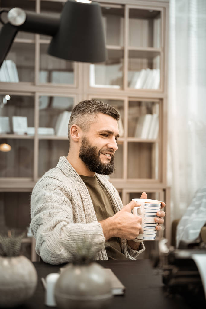 Homme barbu souriant buvant du thé chaud assis au bureau
 - Photo, image