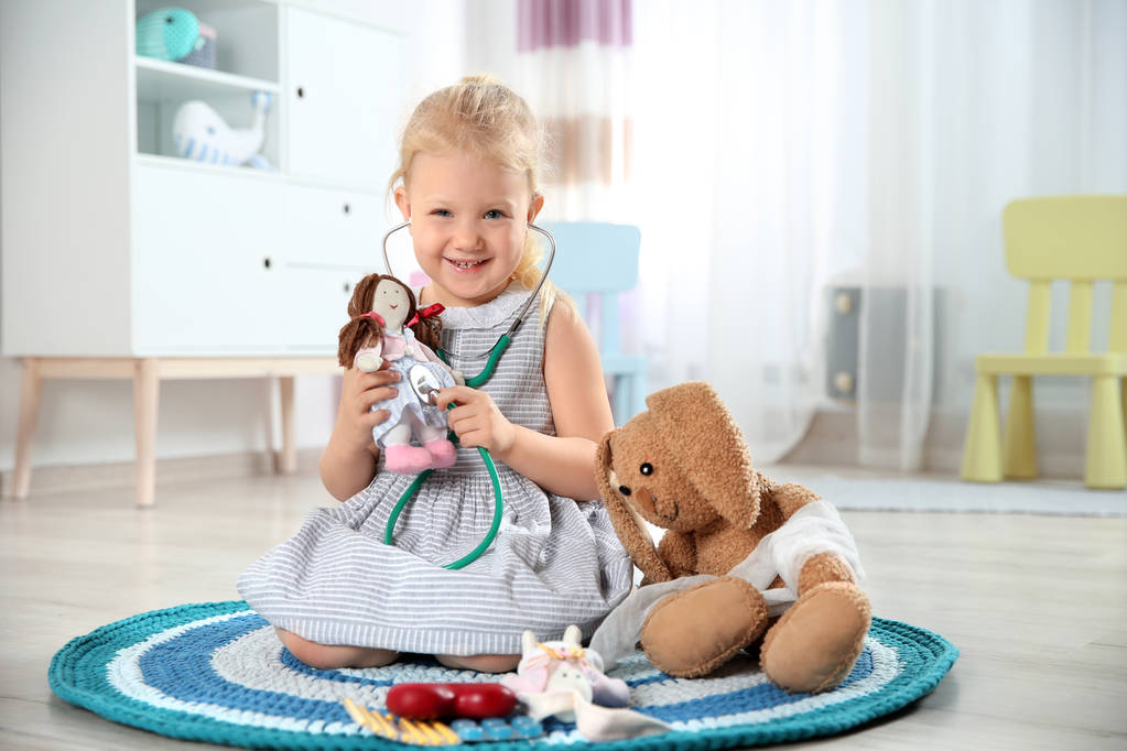 niedliches Kind, das sich beim Spielen mit Stethoskop und Spielzeughasen zu Hause als Arzt vorstellt - Foto, Bild