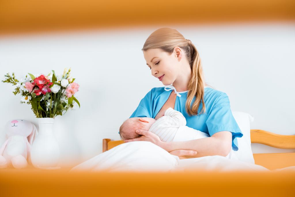 selective focus of happy young mother breastfeeding newborn baby in hospital room - Photo, Image