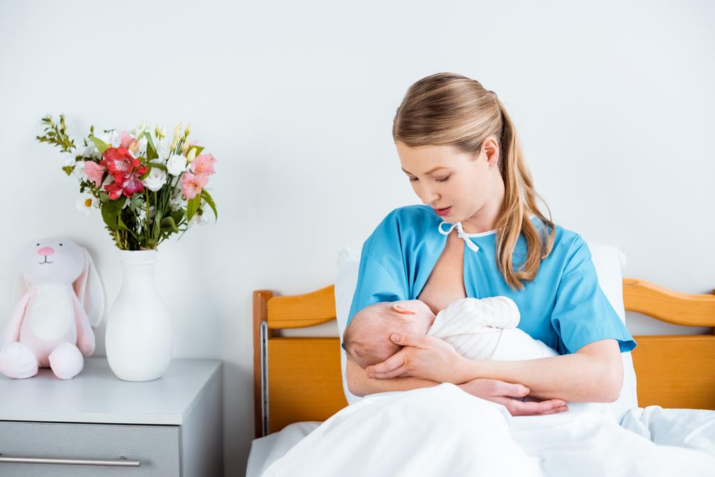jovem mãe sentada na cama e amamentando bebê recém-nascido no quarto do hospital
 - Foto, Imagem