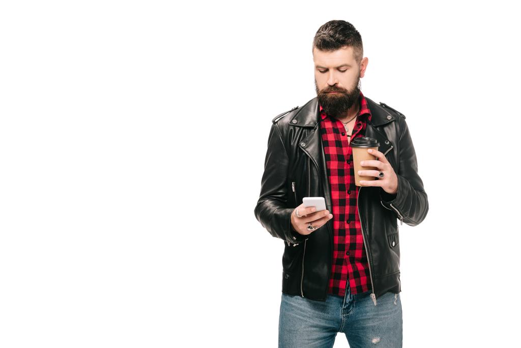γενειοφόρος άνδρας με μαύρο δερμάτινο σακάκι κρατώντας καφέ για να πάει και χρησιμοποιώντας το smartphone, που απομονώνονται σε λευκό - Φωτογραφία, εικόνα