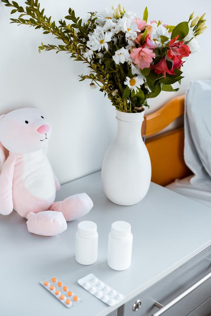 primer plano vista de jarrón con flores, contenedores con pastillas y juguete en la mesa en el hospital
  - Foto, Imagen