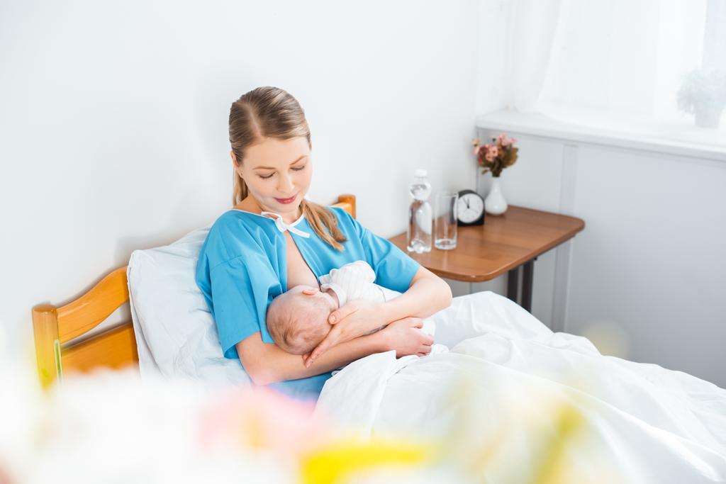 высокий угол зрения счастливой молодой матери грудного вскармливания новорожденного ребенка на кровати в больничной палате
  - Фото, изображение